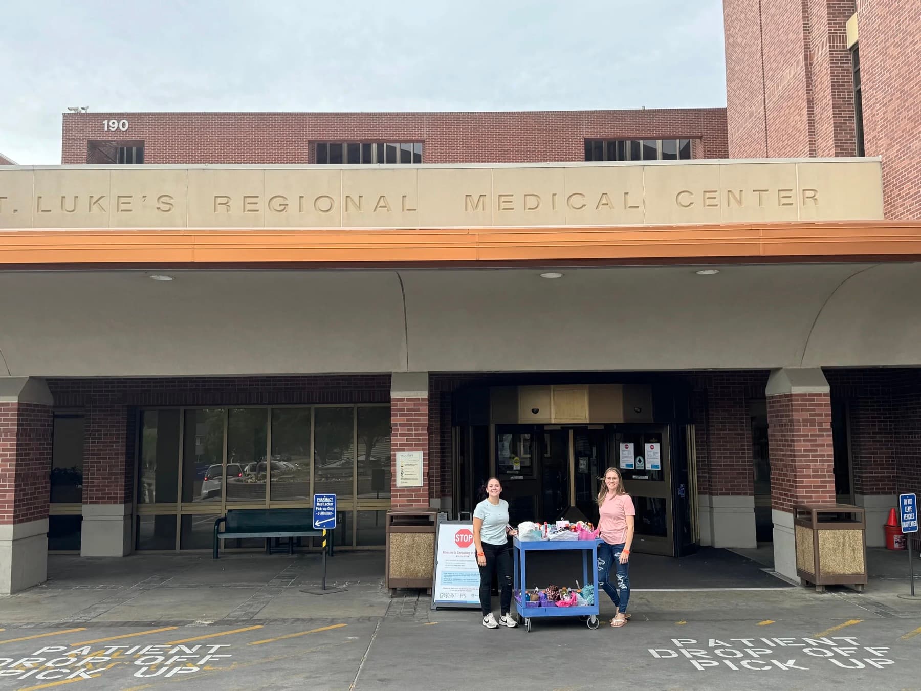 Two volunteers with a cart of care baskets outside a hospital entrance on delivery day